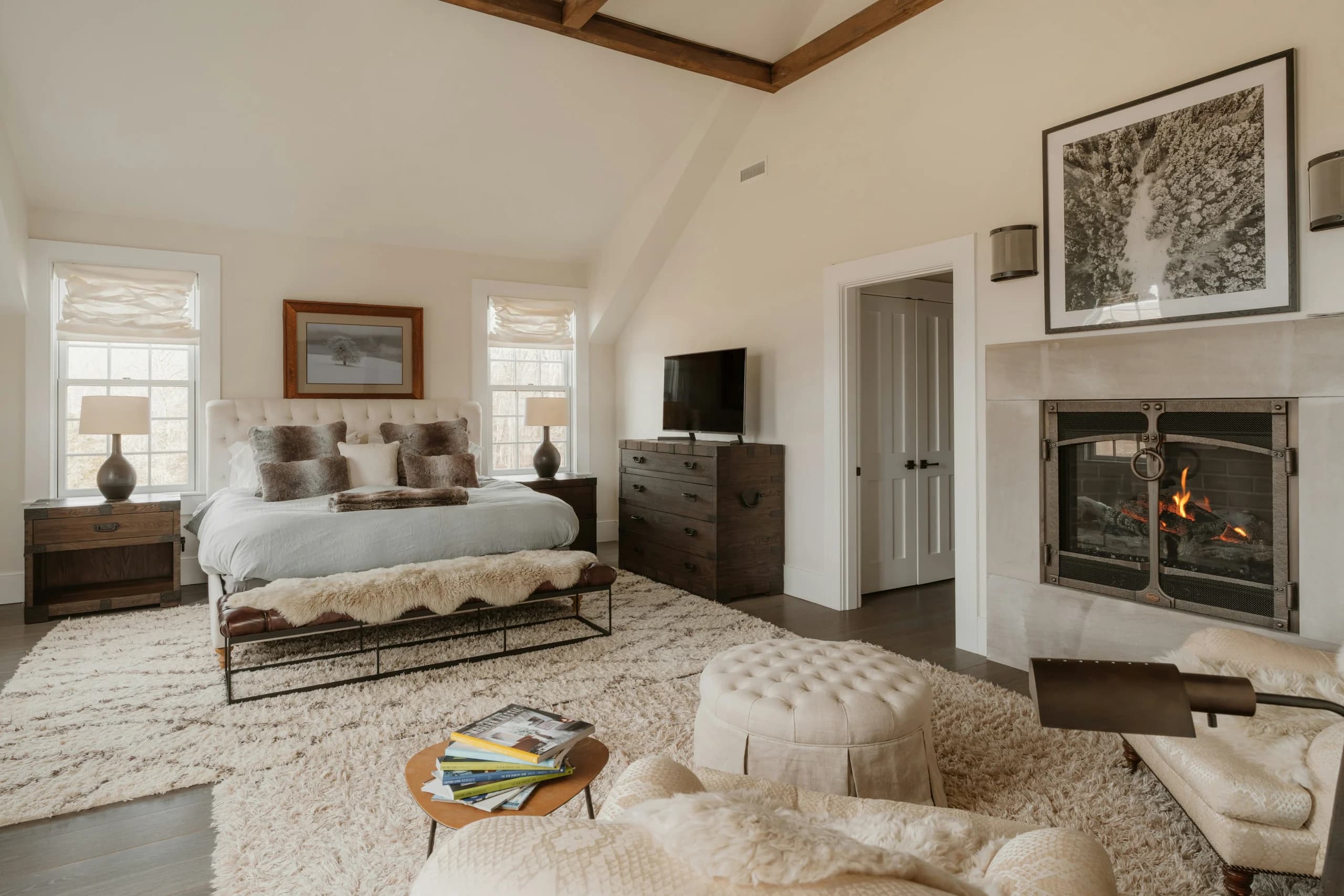 Warm bedroom with an upholstered bed, timber bedside tables and dresser, soft rugs, a fireplace and a separate sitting area